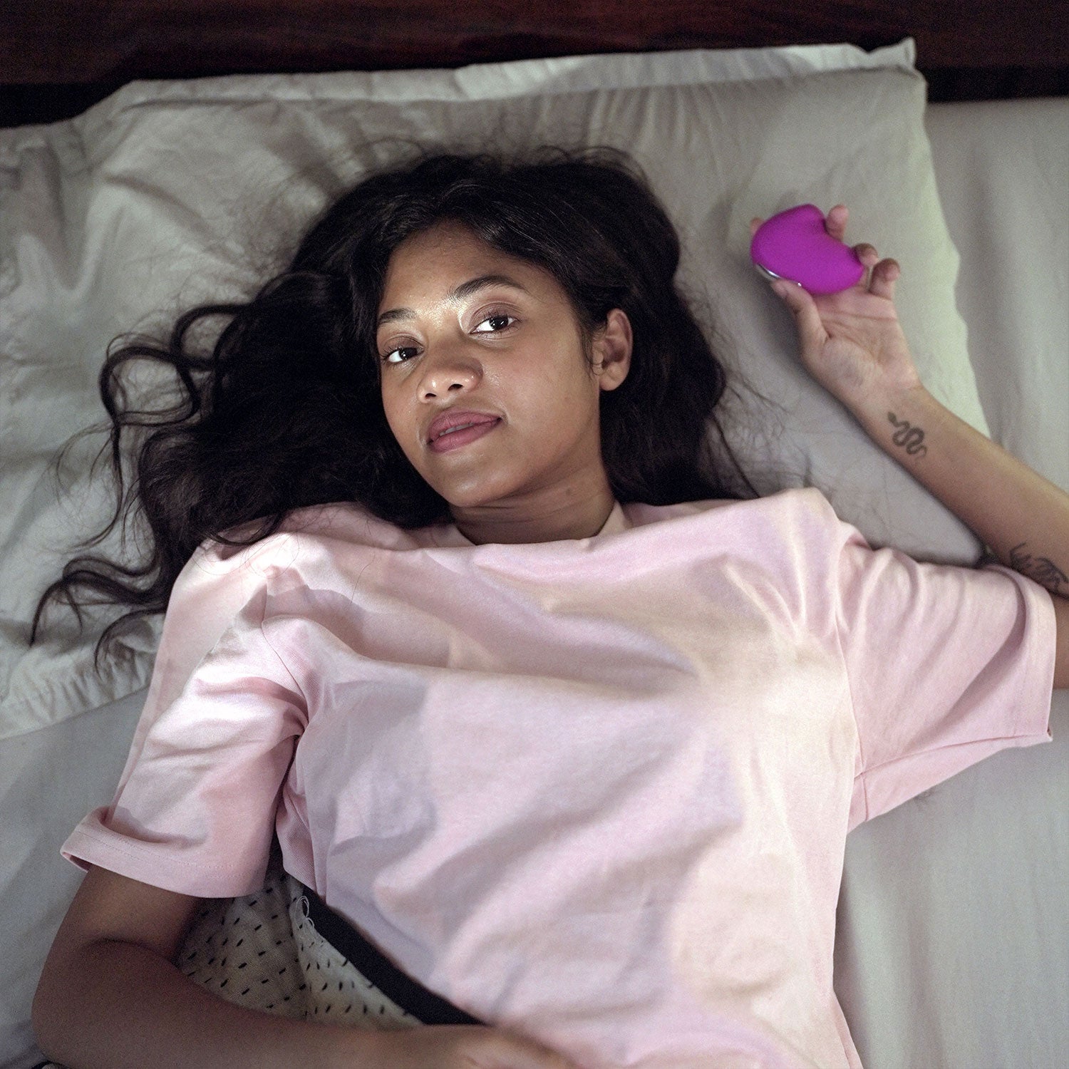 woman in bed holding pink colored lit mini personal massager
