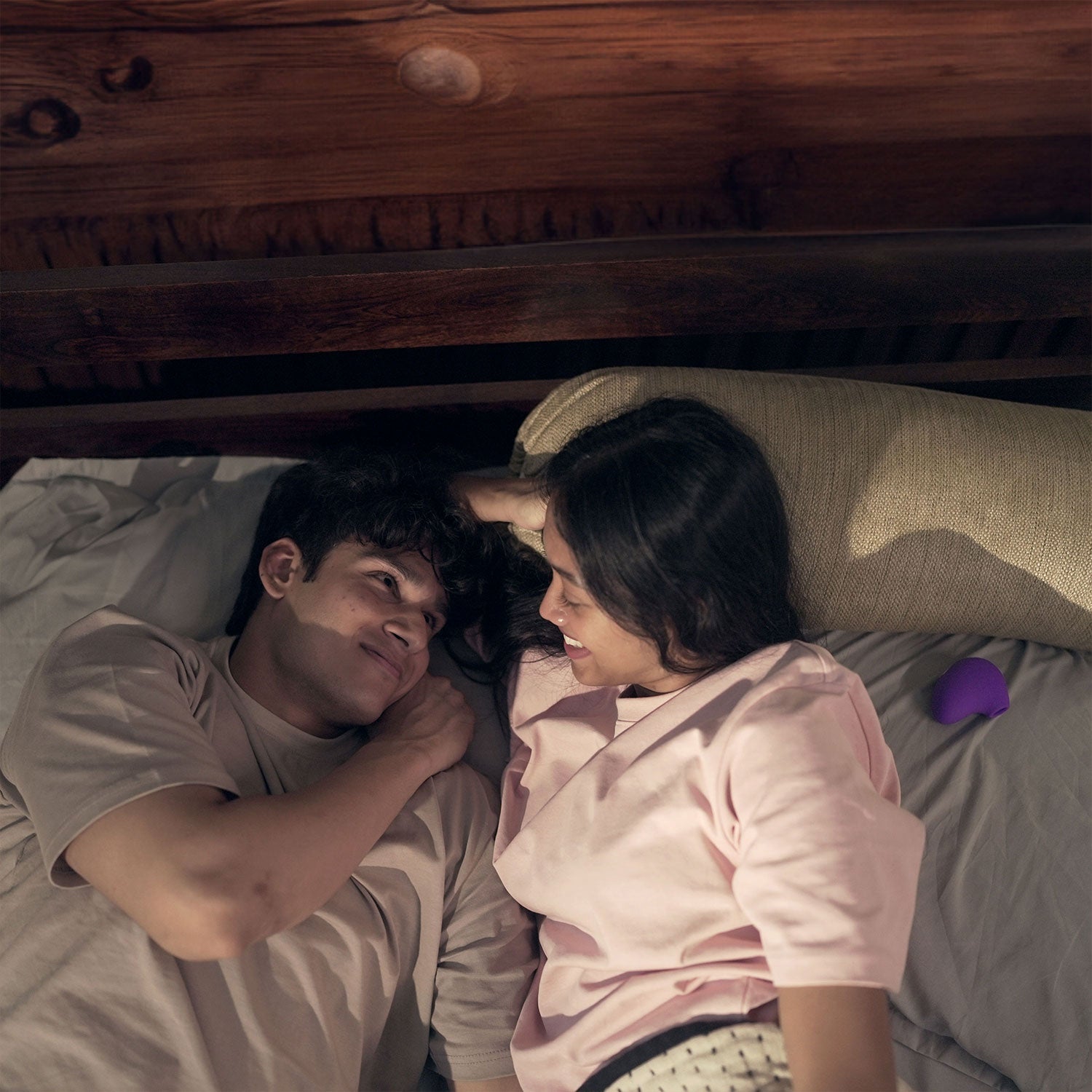 happy couple in bed with violet colored lit massager
