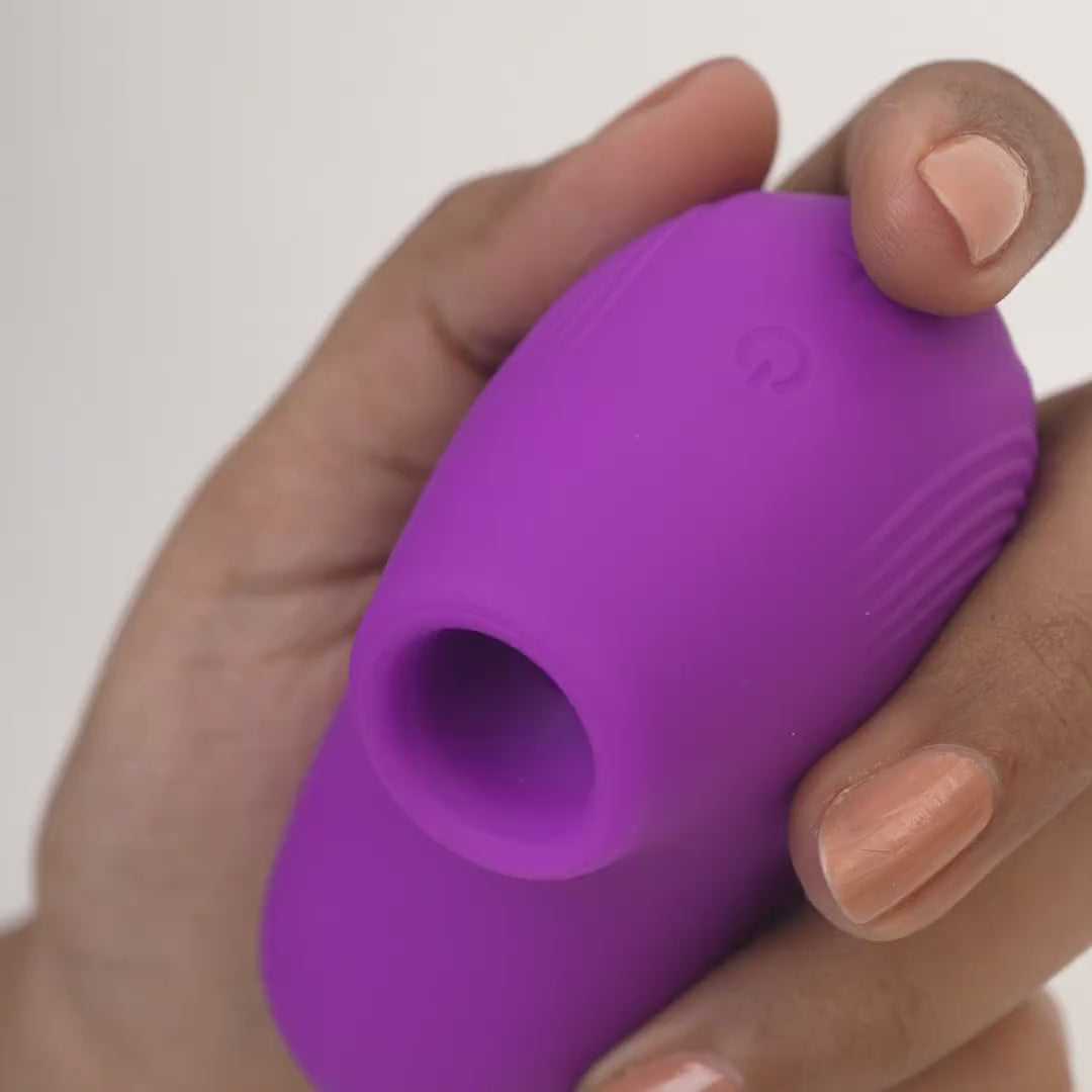 Close-up of LIT suction massager in purple held in hand with plain background.